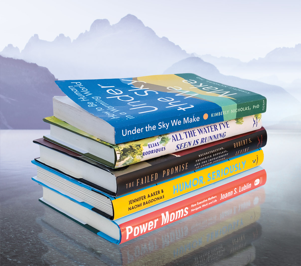 A stack of five books on a table with a mountain backdrop