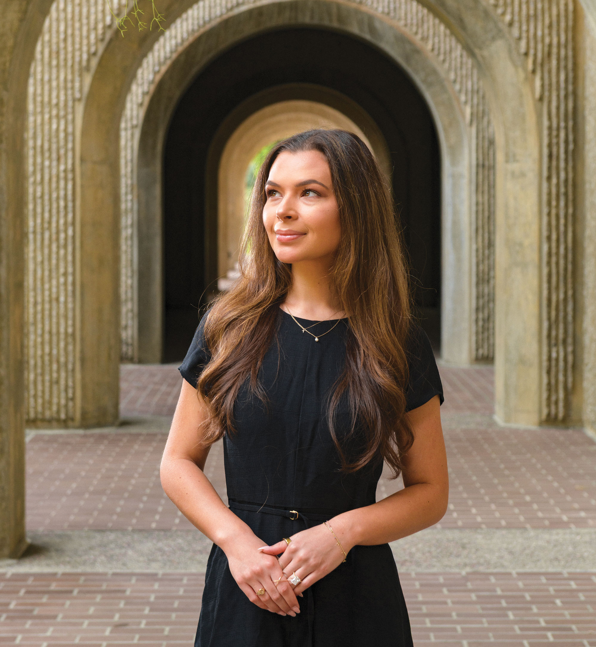 Josie Pearce in a black dress stands beneath stone archways at Stanford Law School.