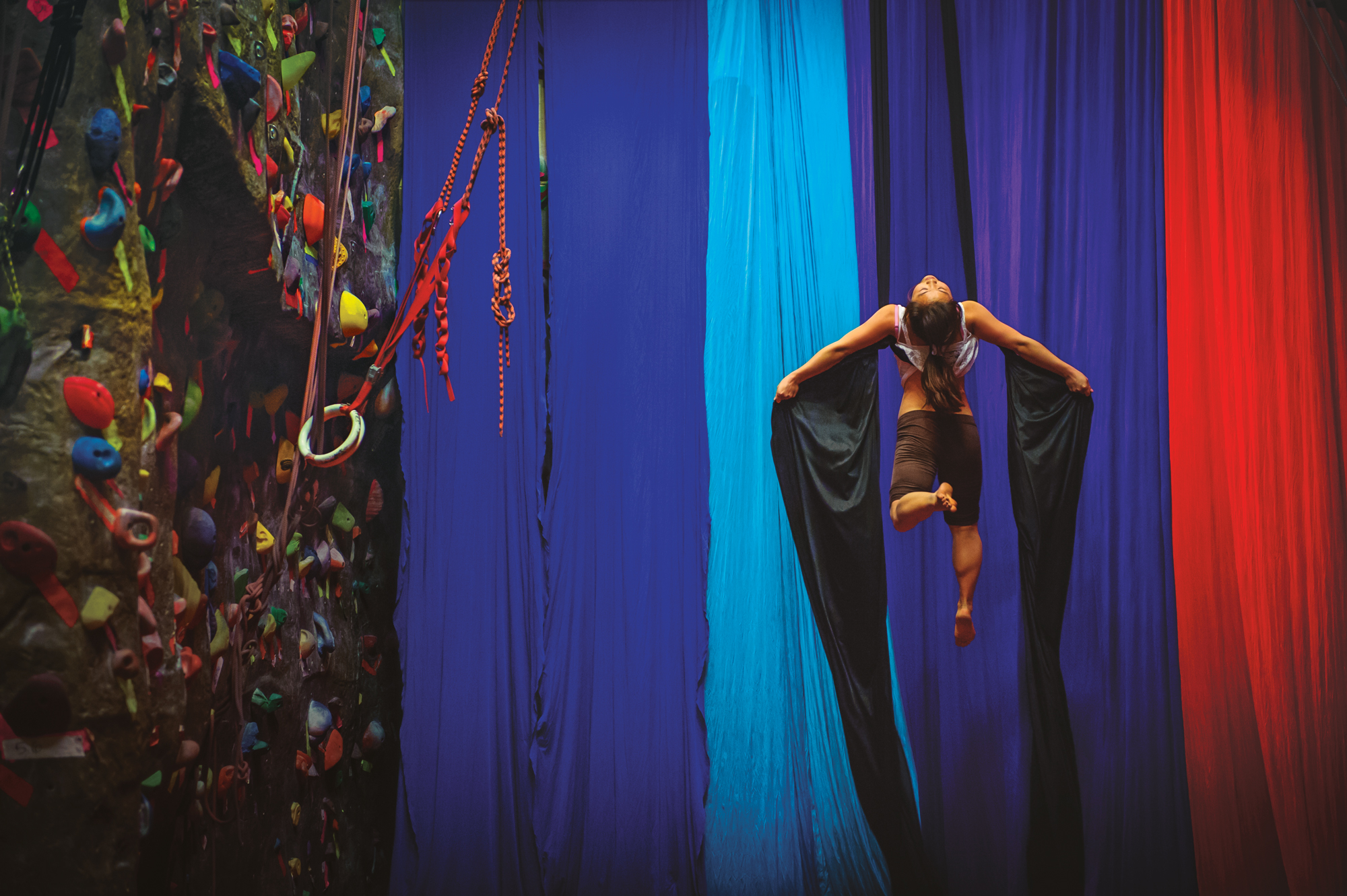 A person doing acrobatics from a set of silky colorful curtains