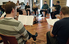 A group of people sitting in a circle, holding sheet music.