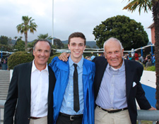 Mack, his father, and his grandfather stand together on campus. Mack is wearing a blue graduation robe.