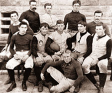 Stanford's pioneer football team. The men are dressed in tight black shirt and white pants, sporting long black socks and shoes.