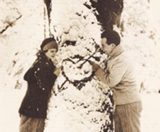 David and Allene together, before Allene's death. They stand on opposite sides of a pine tree, with a heart with an arrow through it drawn over the snowy branches.
