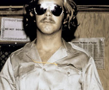 A guard from the Stanford Prison experiment. He wears black aviators and a silky button-down shirt.