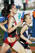 Alicia Follmarr is seen running on the track with blood streaming down her forehead. She sprints alongside another runner.