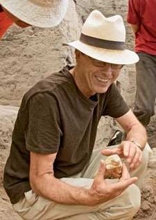 Hodder is crouched down, holding and appreciating some sort of figure. He is accompanied by two people in red shirts.