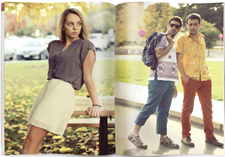 A magazine is shown open. On the left page, a woman in a white skirt and short-sleeved, grey shirt leans against a picnic table. On the right, two trendy men are standing in the street.