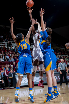 Chiney is up in the air with two opponents. The basketball has just left her hand and it seems clearly to be out-of-reach for the blue-clad defenders.