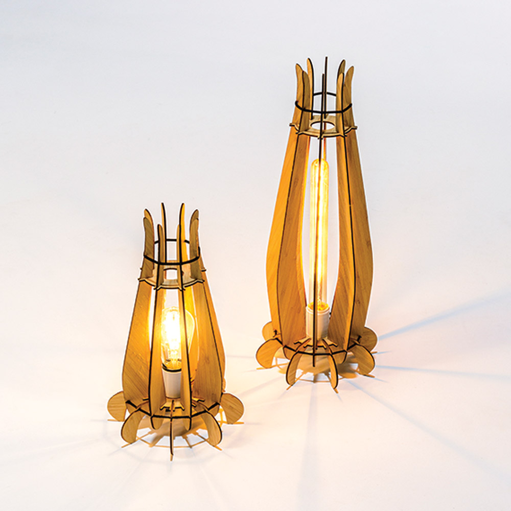 Photograph of two Diya lamps designed by Dinakar. They appear to be about a foot tall and resemble the look of lanterns, shaped somewhat like a tulip before it has opened, somewhat like rockets. They are made of 3D printed wood cutouts that are then constructed.