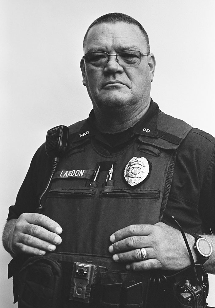 Portrait of a middle-aged police officer in full gear, wearing glasses, and posing.