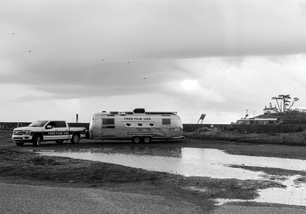 Truck pulling an Airstream trailer across a water puddle.