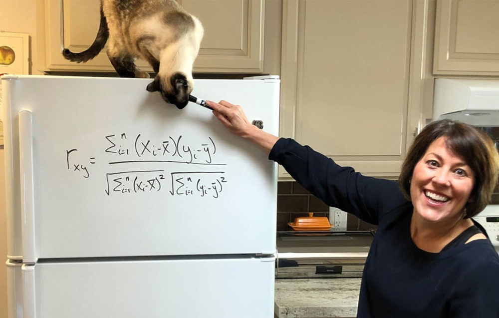 Susan Soule standing next to a refrigerator with an equation written on it and a cat sitting on top
