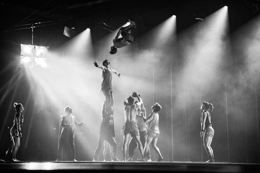 Group of acrobatic performers throwing a tumbler into the air.