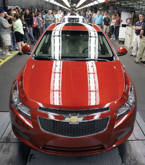 People gather in what appears to be a tunnel. Rows of cars are lined up, the first of which is a sleek red Chevy.