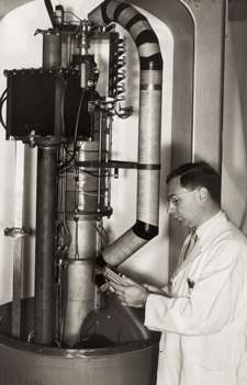 Kaplan stands in front of an large device composed of several metallic tubes and a circular basin.