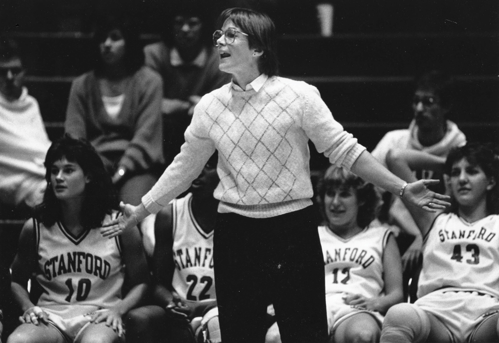 VanDerveer standing in front of players on the bench coaching a game