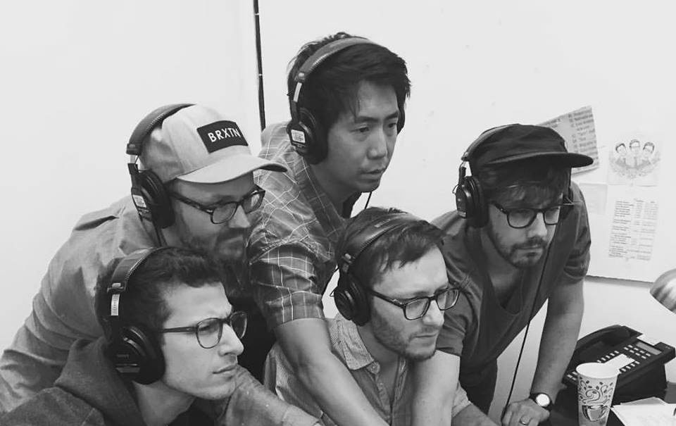 Greg Chun, Andy Samberg and others gathered and staring at a computer.
