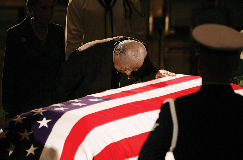 Shultz kneels, head down, with his hand on Reagan's casket.