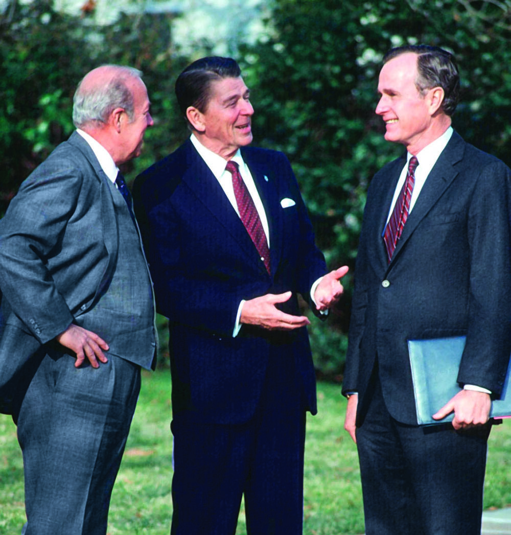 Shultz, Reagan and George H.W. Bush talk outdoors.