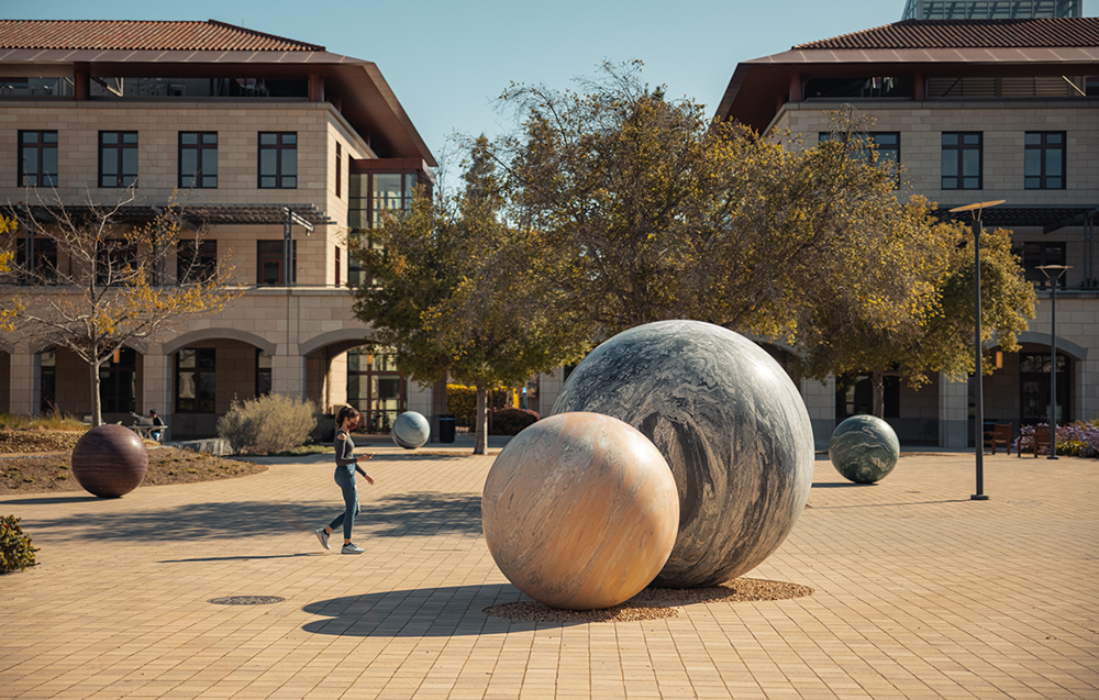 Masked student walking by marble sphere sculptures