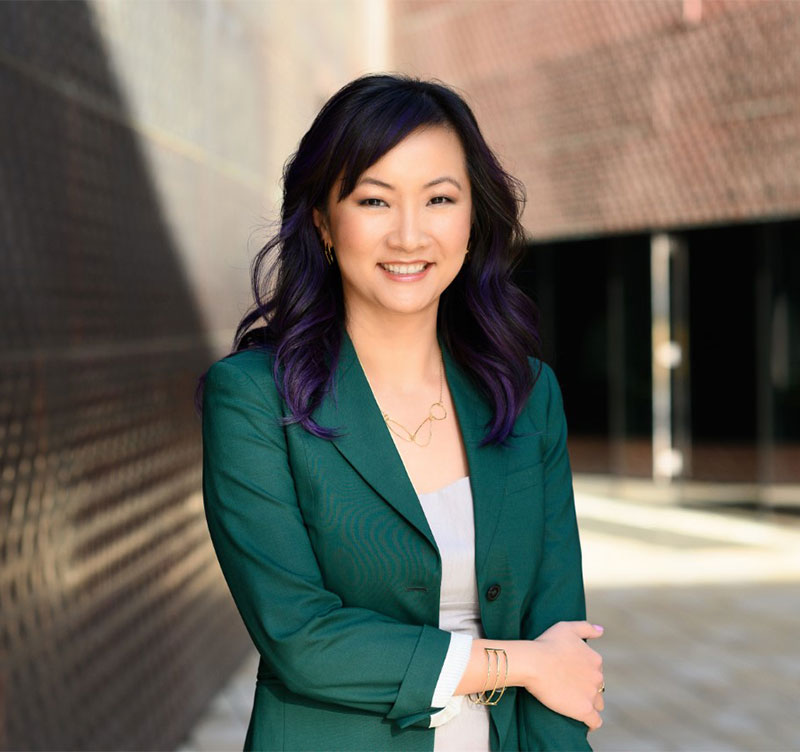 Portrait of a smiling Mamei Sun in between buildings.