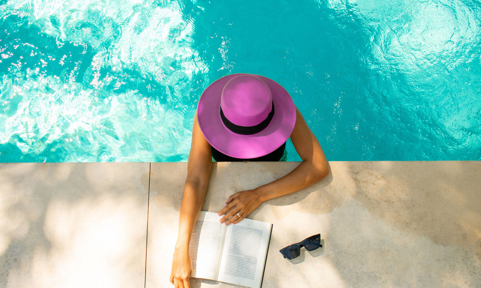 Woman wearing hat in pool reading a book