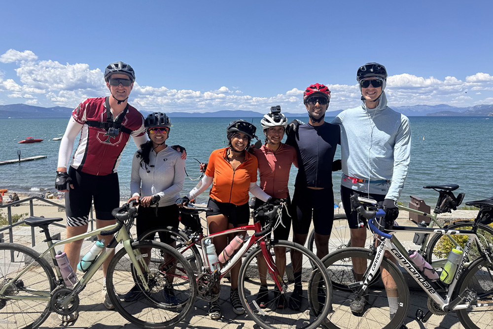 Six people standing with bikes in front of a body of water