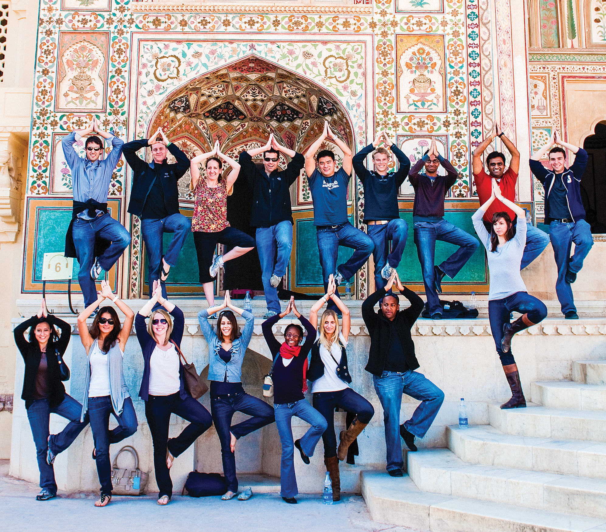 17 students in yoga poses in front of an ornate building.