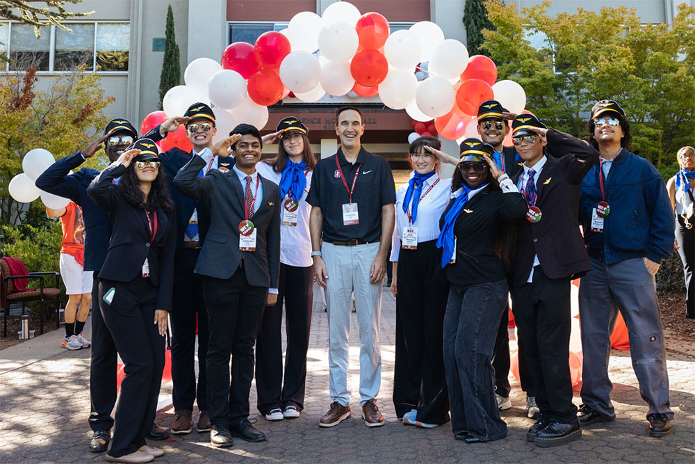 Residential staff, dressed as airline pilots and gathered around President Levin, salute.