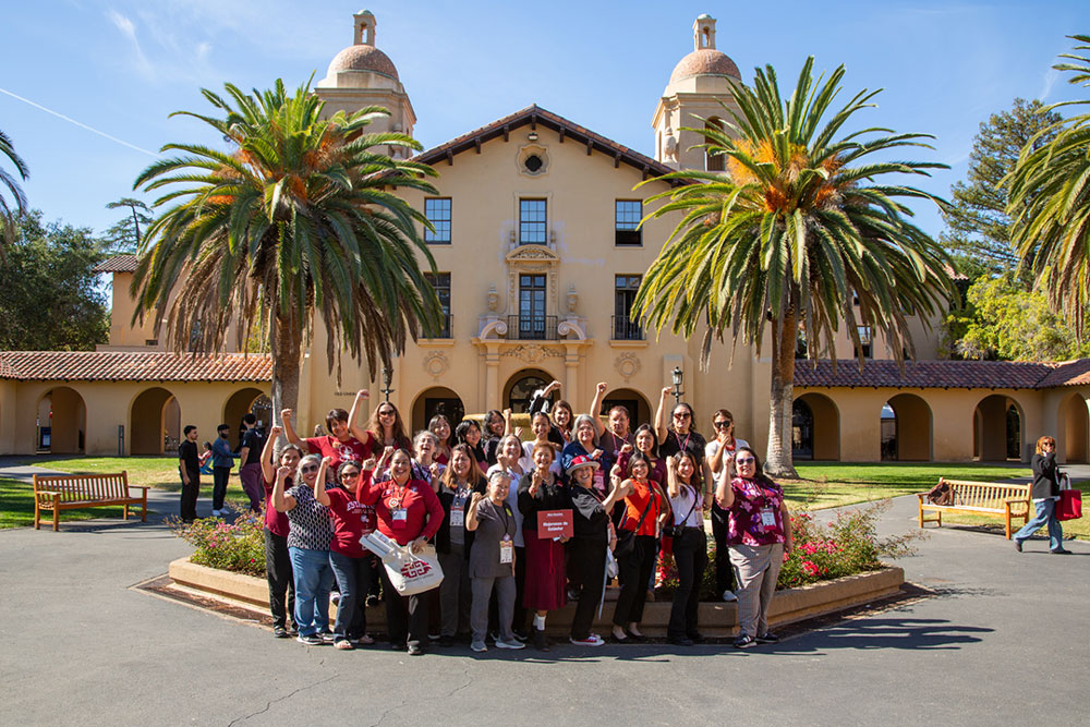 Group of about 25 women standing in front of Old Union with their arms raised.
