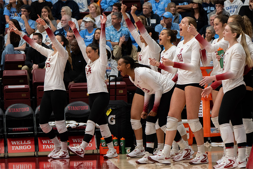 Members of the women's volleyball team cheering on the sidelines with the crowd behind them