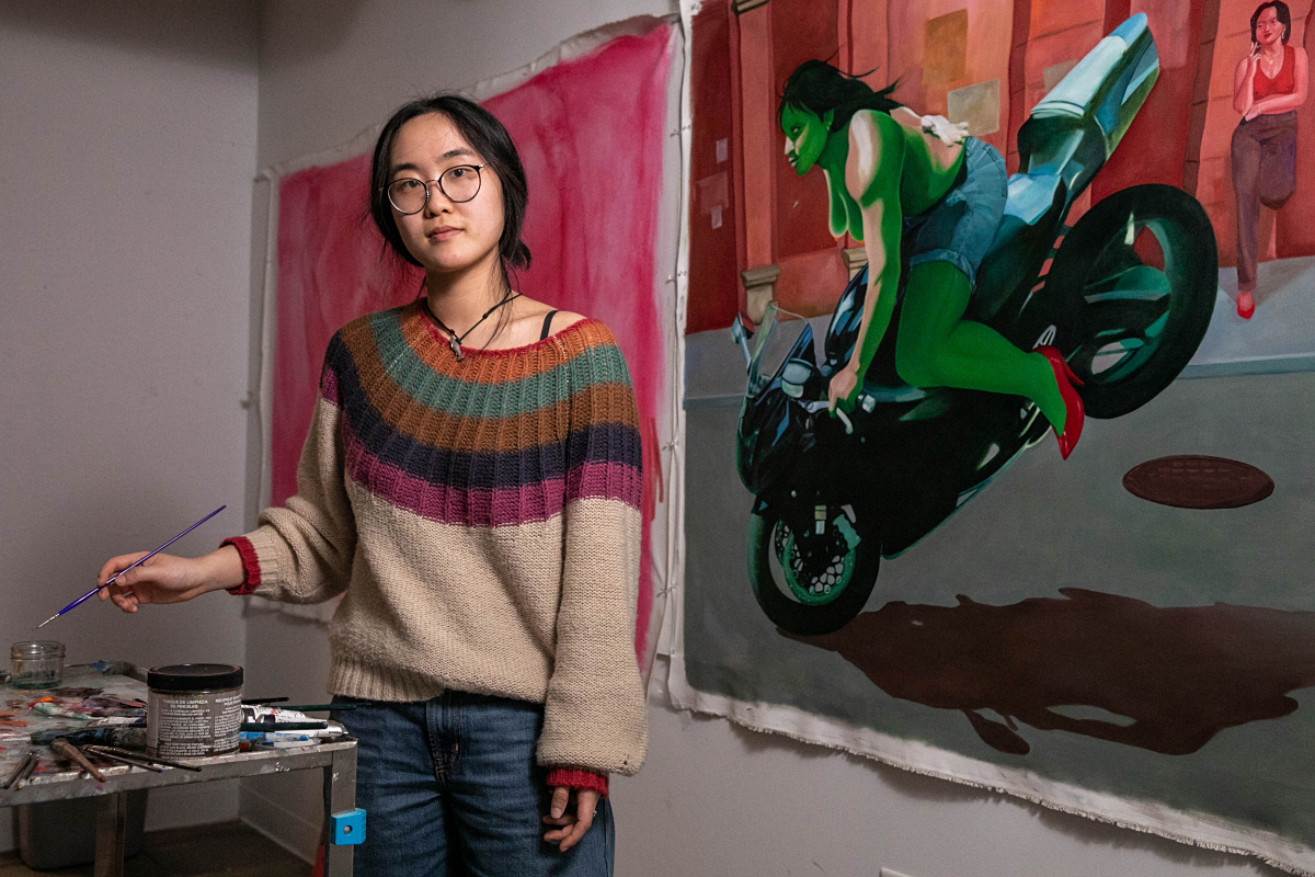 Song Wu standing next to a painting of a woman on a motorcycle