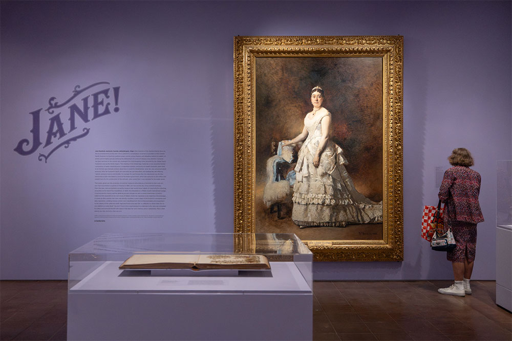 A room with purple walls where Jane Stanford's portrait hangs and a woman looking at it